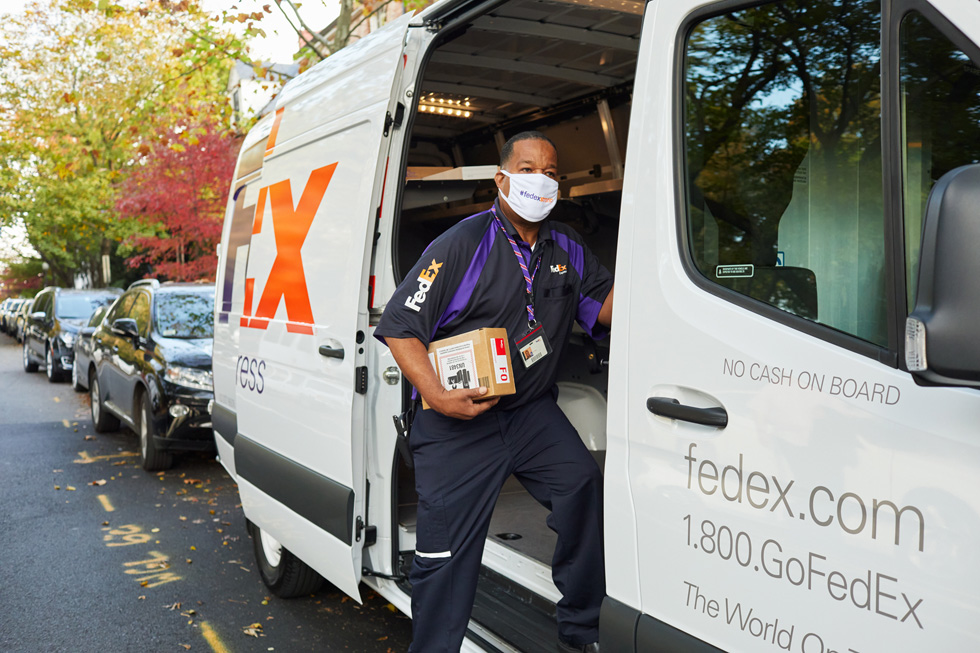 Сотрудник FedEx доставляет посылку Apple из автофургона FedEx.